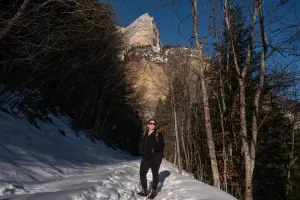 Mulher de óculos escuro em trilha nevada em frente aos Alpes.