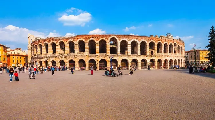 Turistas em frente à Arena de Verona em dia de céu azul na cidade romântica.