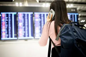 Mulher olhando painel de aeroporto, falando ao celular.
