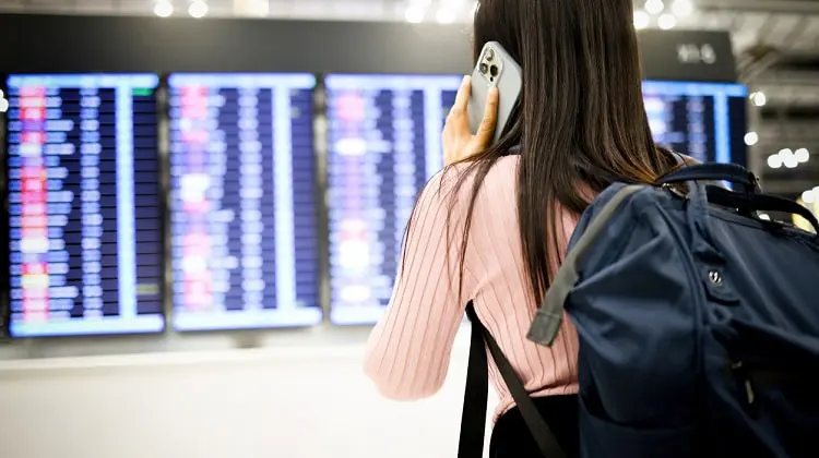 Mulher olhando painel de aeroporto, falando ao celular.