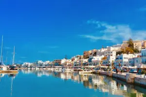 uma vista magnífica, num dia de sol, com um mar com água muito azul, casas brancas refletindo nele e barcos ancorados