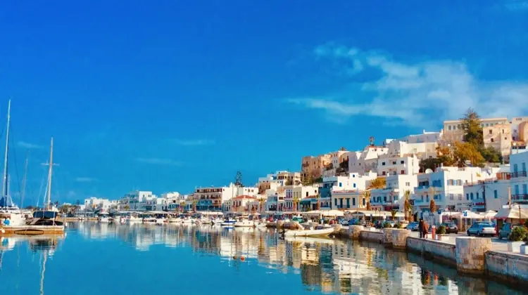 uma vista magnífica, num dia de sol, com um mar com água muito azul, casas brancas refletindo nele e barcos ancorados