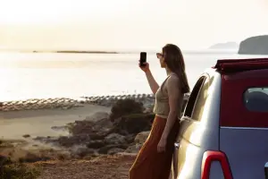 Mulher com o celular na mão, encostada em um carro, tirando foto da paisagem