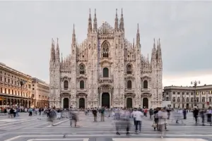 Foto do Duomo de Milão de frente, com pessoas passando, em dia nublado