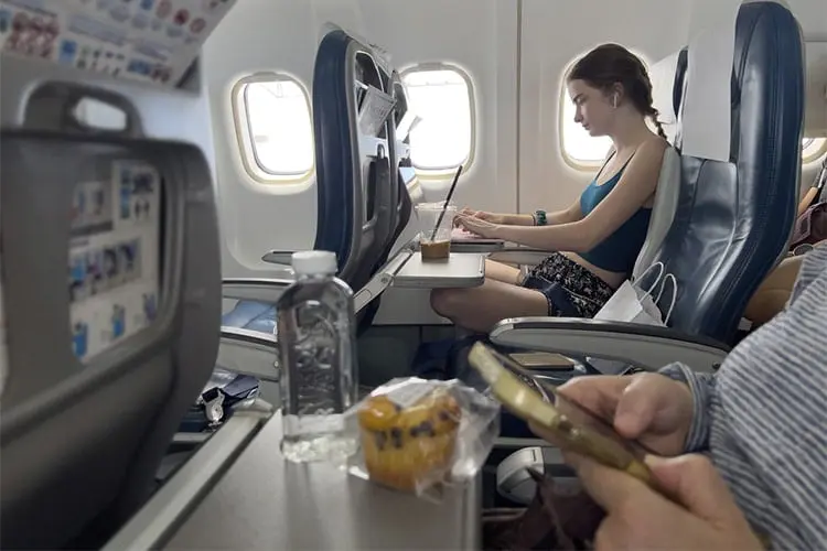 Imagem de pessoas usando eletrônicos em mesinha retrátil de avião