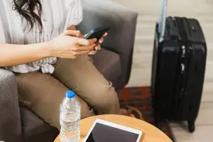 mulher usando o celular com mala de viagem ao lado