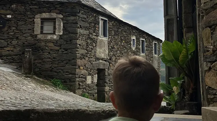Menino olha para casa tradicional de pedra.