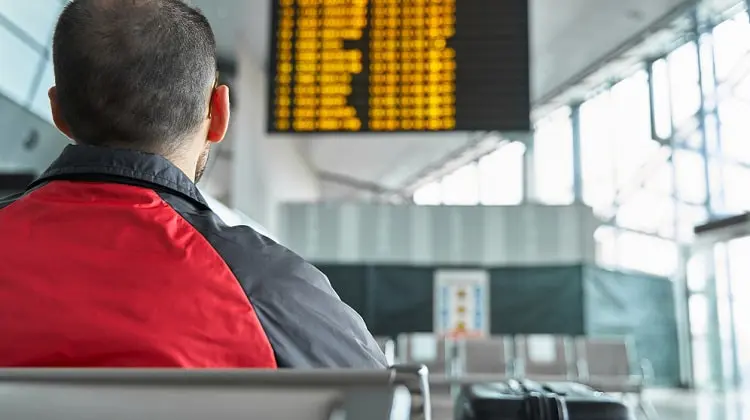 Pessoa que, ao sofrer atraso de voo, está olhando painel de aeroporto