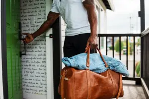 Homem, após fazer reserva de hotel, entrando em quarto com mala na mão.