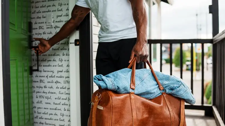 Homem, após fazer reserva de hotel, entrando em quarto com mala na mão.