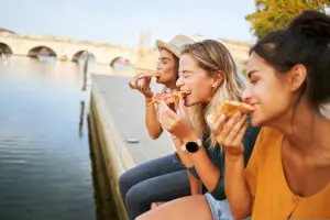 Três mulheres comendo pizza na beira de um rio