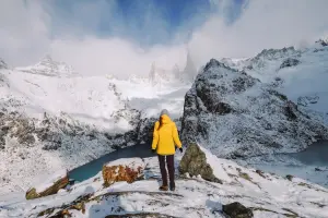 Mulher com jaqueta adequada para enfrentar o frio do alto de uma montanha nevada na Europa.