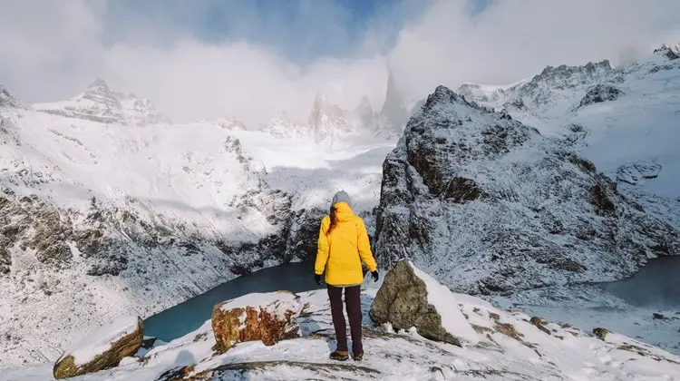 Mulher com jaqueta adequada para enfrentar o frio do alto de uma montanha nevada na Europa.