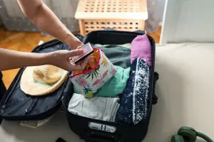 Mulher organizando necessaire de viagem sobre mala já feita.