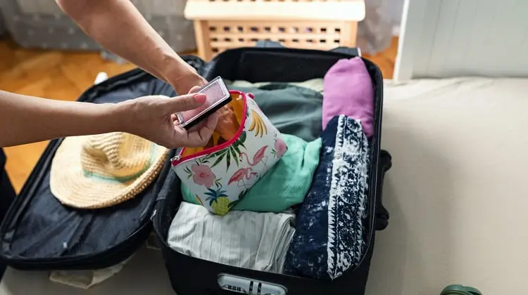 Mulher organizando necessaire de viagem sobre mala já feita.