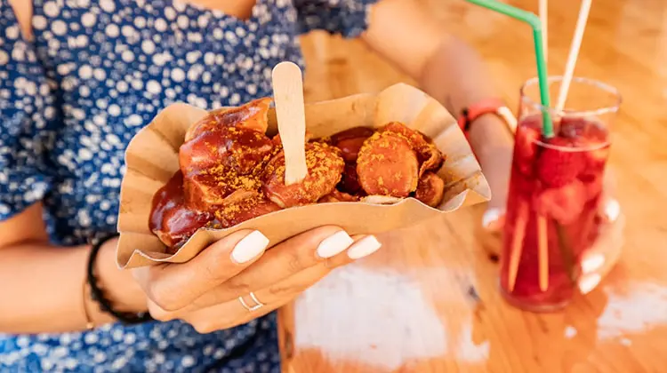 Mulher segurando currywurst e bebida onde comer em Berlim