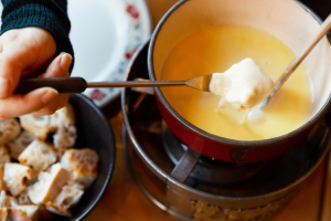 Pessoa mergulhando pão no fondue, um dos pratos tradicionais mais conhecidos da Suíça