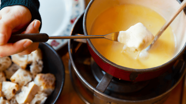 Pessoa mergulhando pão no fondue, um dos pratos tradicionais mais conhecidos da Suíça