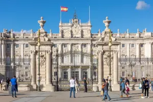 Vista frontal do Palácio Real de Madrid, em dia de sol, com bandeira da Espanha, em dia de sol