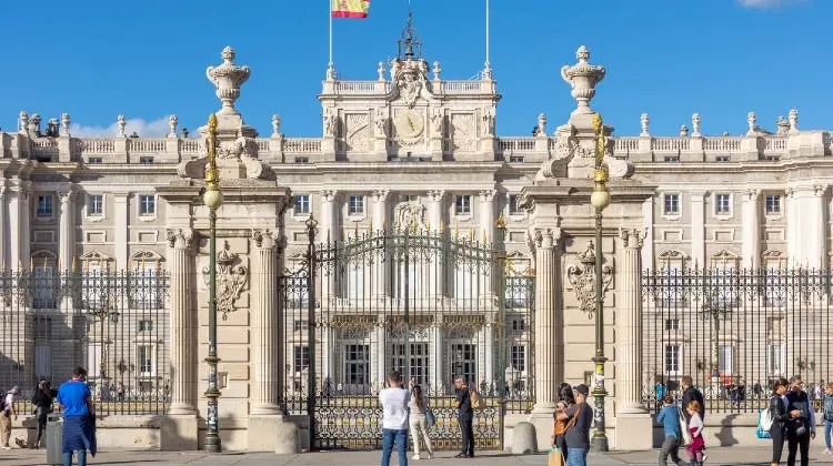 Vista frontal do Palácio Real de Madrid, em dia de sol, com bandeira da Espanha, em dia de sol