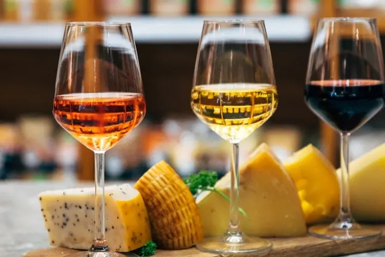 Três taças de vinhos diferentes acompanhadas de pedaços de queijos em um restaurante.