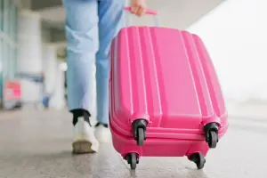 Mulher carregando mala de rodinhas rosa em aeroporto.
