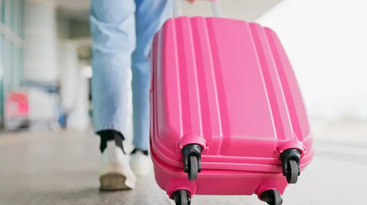 Mulher carregando mala de rodinhas rosa em aeroporto.