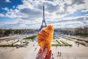 Pessoa com um prato típico da França, em frente a Torre Eiffel.