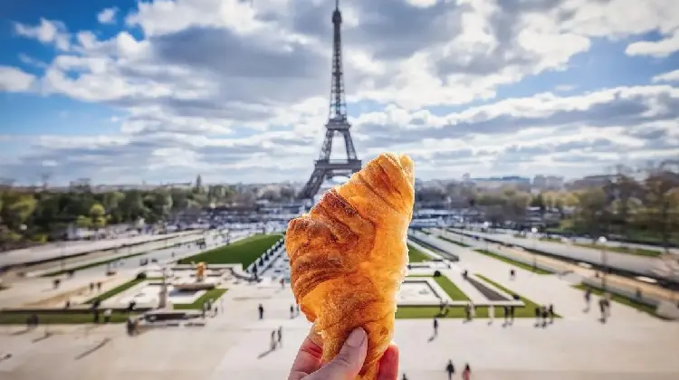 Pessoa com um prato típico da França, em frente a Torre Eiffel.