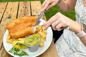 Mulher cortando peixe com fritas.