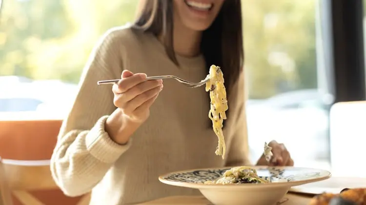 Mulher feliz comendo um prato de espaguete.
