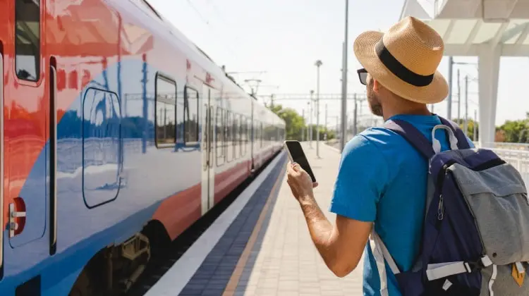 Turista com celular na mão em estação de trem