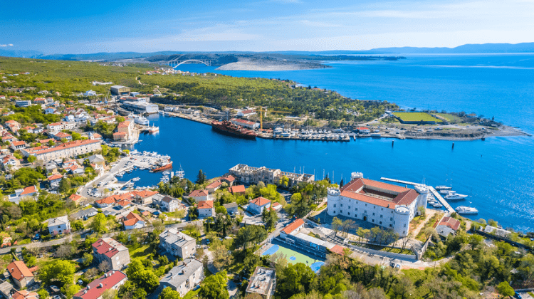 Cidade litorânea da Croácia com casas de telhados vermelhos e um porto ao fundo