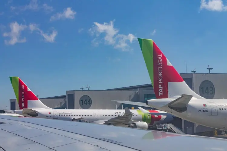 Aviões da TAP parados no pátio de um aeroporto de Portugal, de dia. Somente a TAP oferece passagem aérea para Porto com voos diretos para a cidade.