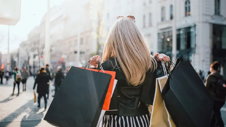 Mulher com sacolas de compras anda pela ruas
