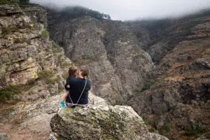 Mãe e filha sentadas em pedra observando as montanhas de Ermelo ao longe em dia nublado.