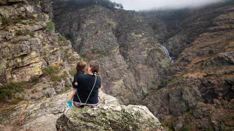 Mãe e filha sentadas em pedra observando as montanhas de Ermelo ao longe em dia nublado.