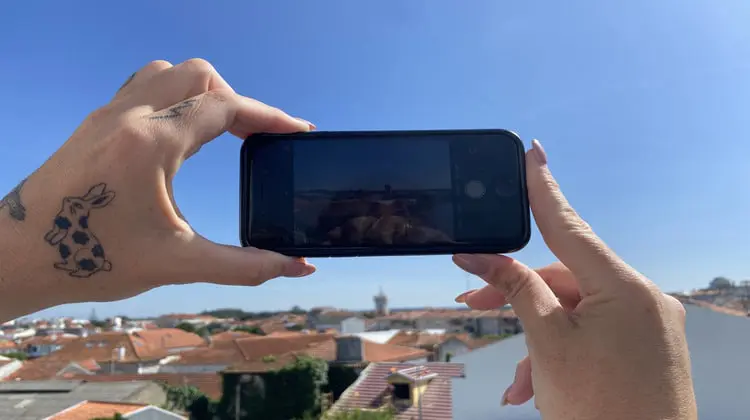 Mãos segurando telefone sobre vista a ser fotografada.