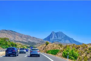 Estrada espanhola com carros passando e uma montanha ao fundo