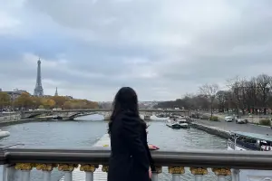 Mulher observa Paris em dia nublado próximo ao Rio Senna com Torre Eiffel ao fundo