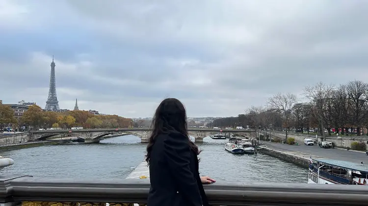 Mulher observa Paris em dia nublado próximo ao Rio Senna com Torre Eiffel ao fundo
