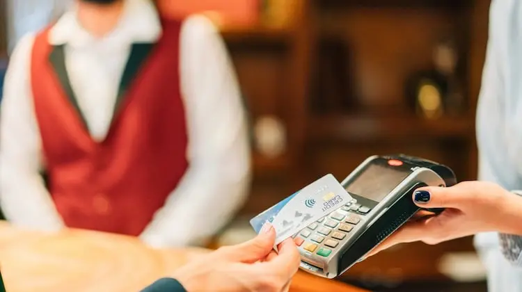 Mulher pagando com cartão via aproximação com o cartão Visa Travel Money na máquina de cartão
