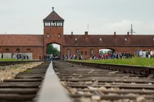 Trilhos de trem com visitantes ao fundo no campo de concentração da Polônia, Auschwitz II-Birkenau