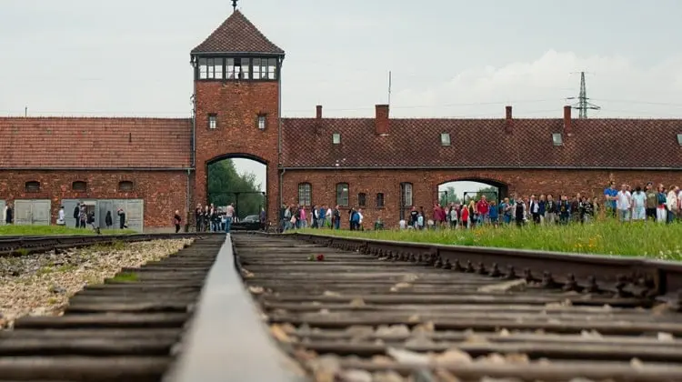 Trilhos de trem com visitantes ao fundo no campo de concentração da Polônia, Auschwitz II-Birkenau