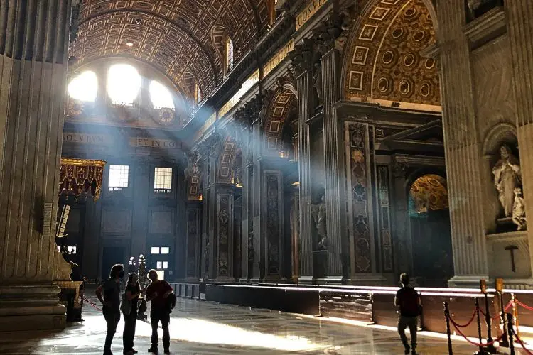 Interior da Basílica de São Pedro no Vaticano, com raios de luz entrando pelas janelas.