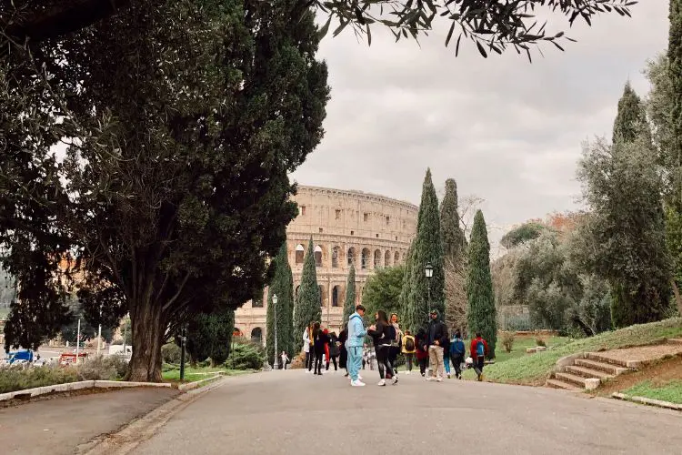 Pessoas caminhando pelo jardim com vista para o Coliseu em Roma.