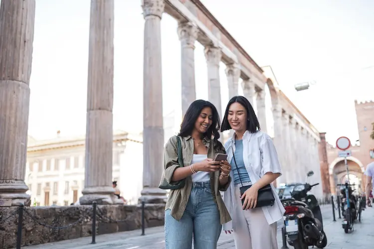 Duas amigas usam celular para aproveitar a viagem em Milão, na Itália.
