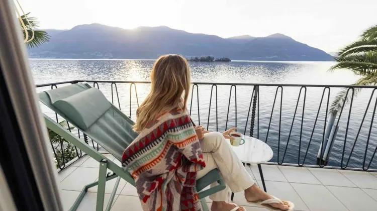 Na varanda, mulher toma café enquanto observa a paisagem