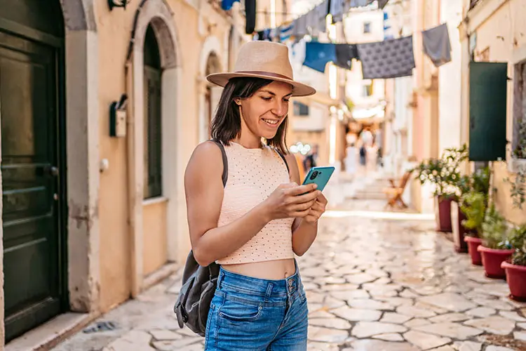 Mulher sorrindo enquanto usa o celular em uma rua de cidade europeia.