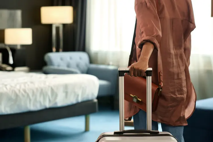Mulher segurando mala de viagem entrando em quarto de hotel